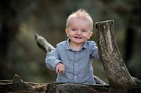 a baby boy is standing on a log in a forest