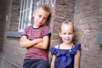 two children leaning against a brick wall