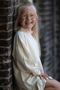 a little girl wearing glasses is sitting on a brick wall