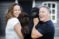 a man and woman are holding two black puppies