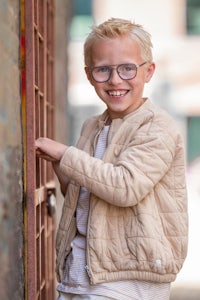 a boy wearing glasses and a jacket leaning against a wall