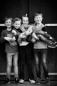 a black and white photo of four boys posing in front of a wooden door