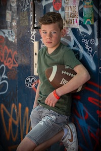 a boy leaning against a wall holding a football