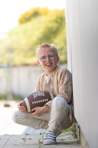 a young boy holding a football in front of a wall