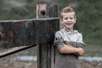 a young boy is leaning against a wooden fence